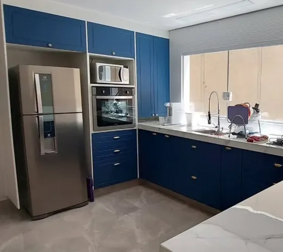 Cozinha planejada com armários azuis até o teto, torre de forno e micro-ondas e bancada em mármore